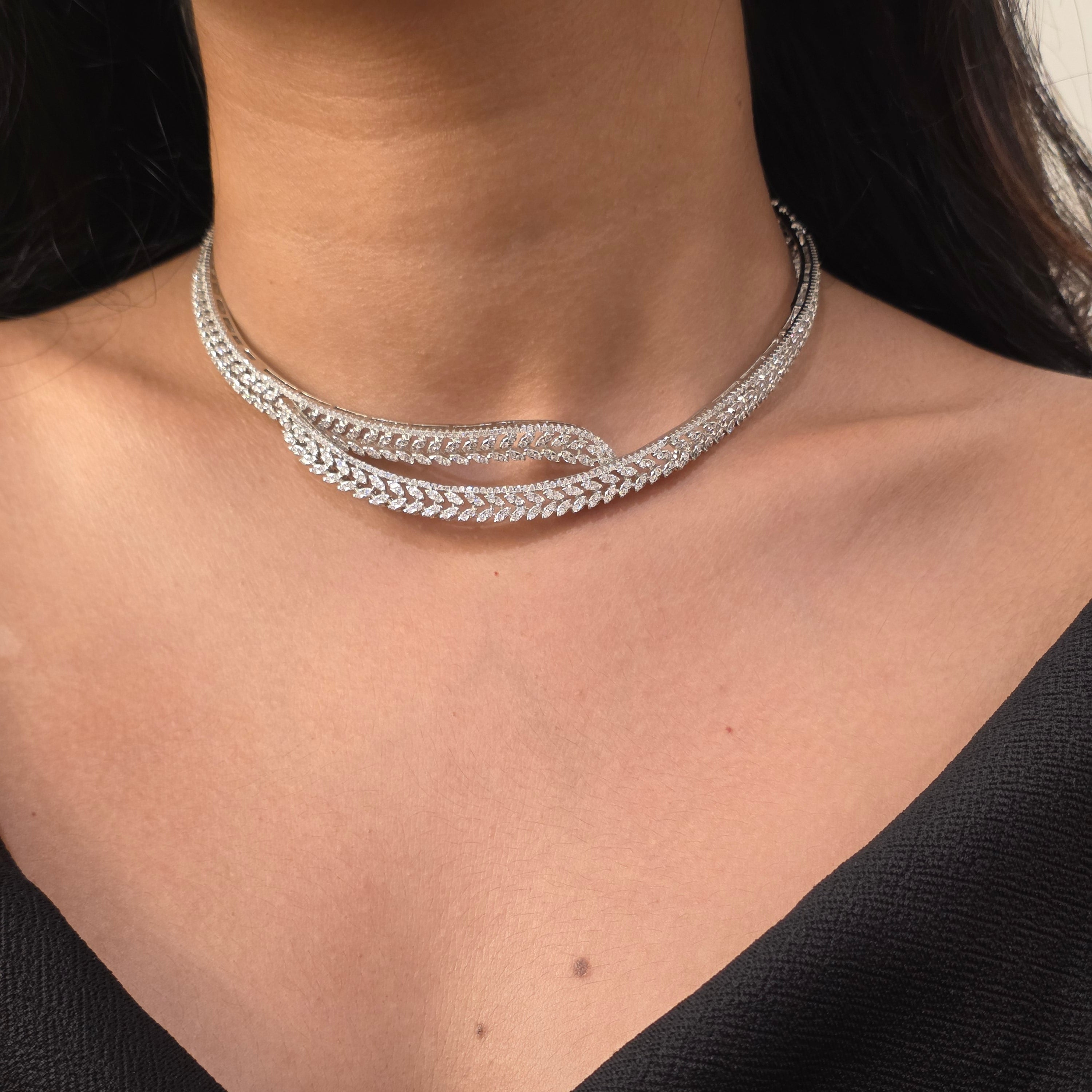 A close-up of a person's neck and upper chest wearing a silver-toned double-strand chain choker necklace with pavé-set clear stones, paired with a black top.