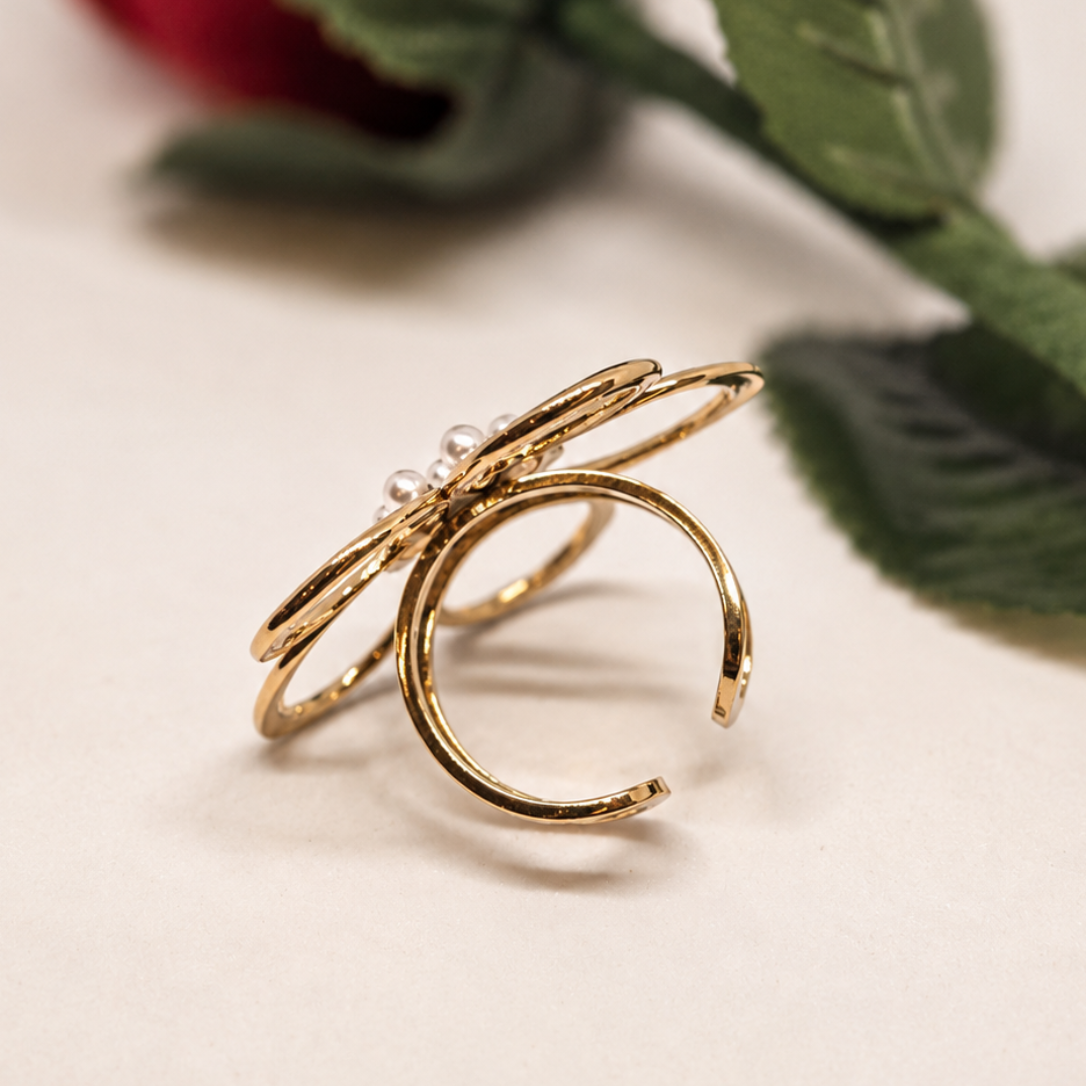 A pair of gold-toned adjustable rings with a small clear stone detail, displayed on a light beige surface with a blurred red rose in the background.