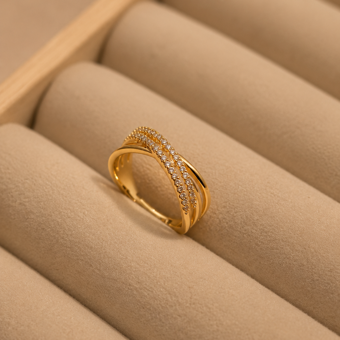 A gold ring with two rows of small clear stones, displayed on a beige jewelry box cushion.