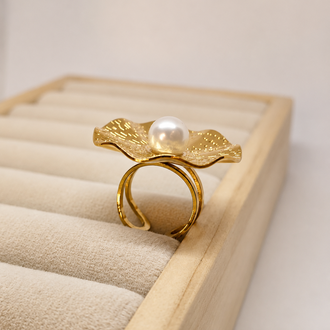 A gold ring designed to look like a flower with textured petals and a central white pearl, displayed on a beige velvet jewelry organizer tray.