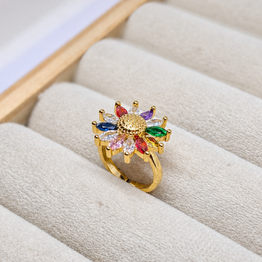 A gold ring with a colorful flower-like setting, displayed on a beige velvet jewelry box.