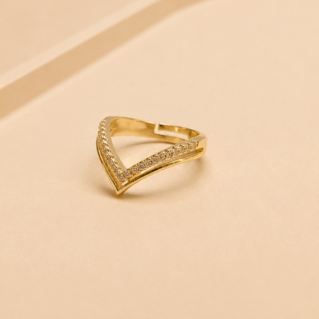 A gold triangular ring with pavé-set clear stones on a warm beige background.