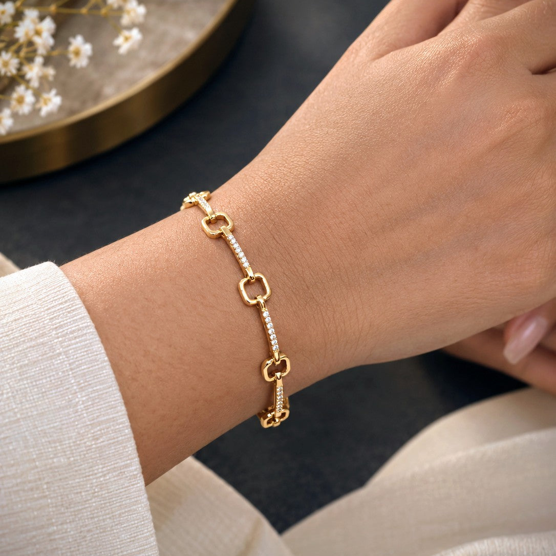 A delicate gold chain bracelet with rectangular links and small pavé-set clear stones, shown worn on a person's wrist. The bracelet features one larger open rectangular link and one key-shaped link at the end.