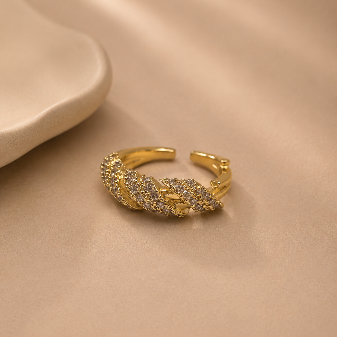 A gold-toned open ring earring adorned with pavé-set clear stones, displayed on a soft beige satin fabric background.