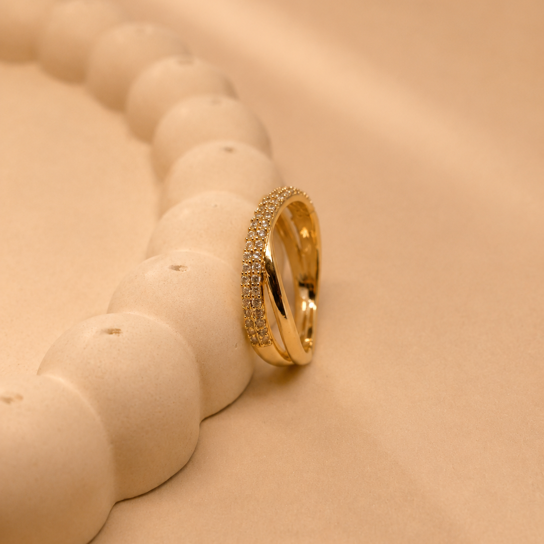 A gold ring with a textured pavé band, resting on a beige surface next to a white ceramic beaded tray.
