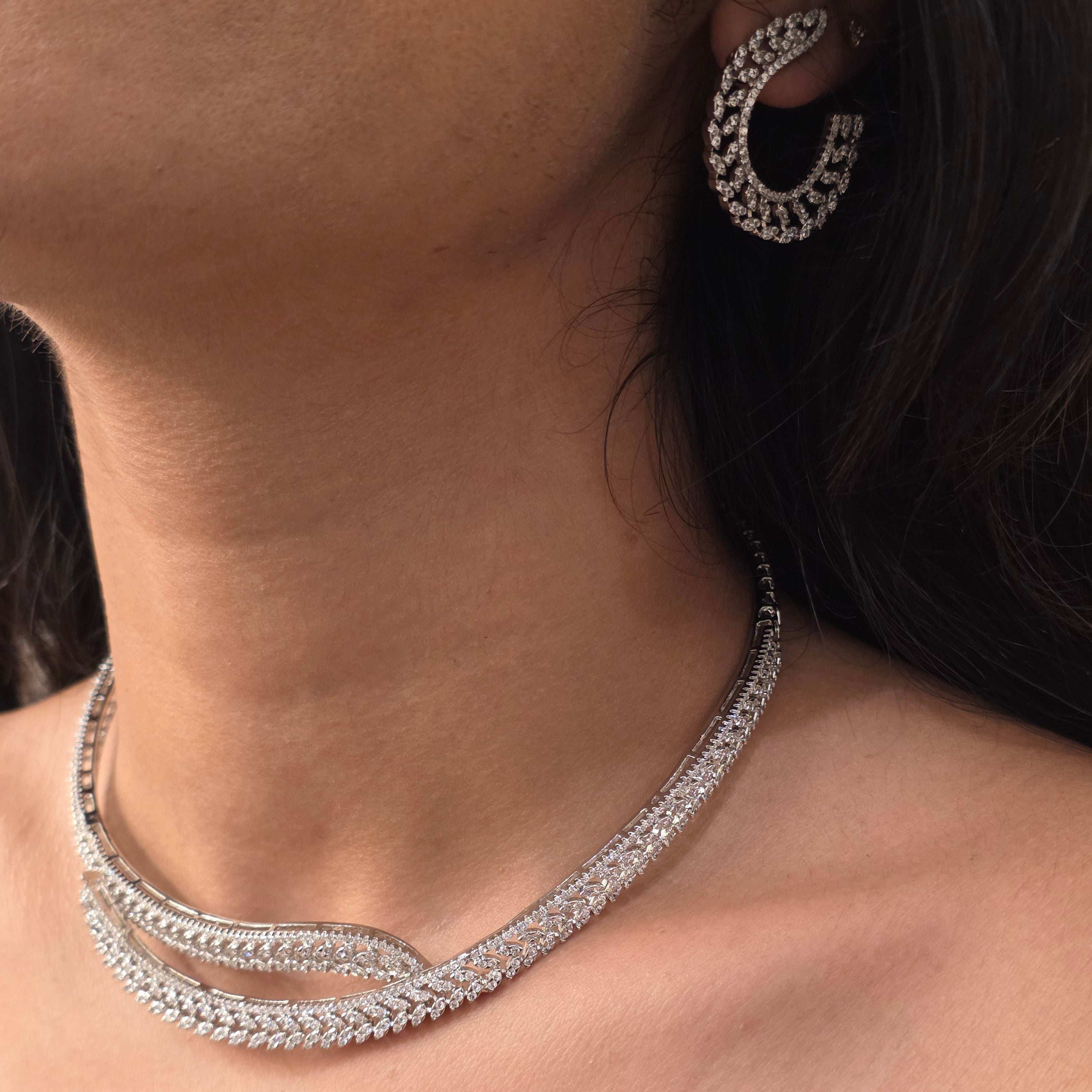 A close-up of a model's neck and ear wearing a silver-toned, multi-strand pavé necklace and matching curved hoop earring.