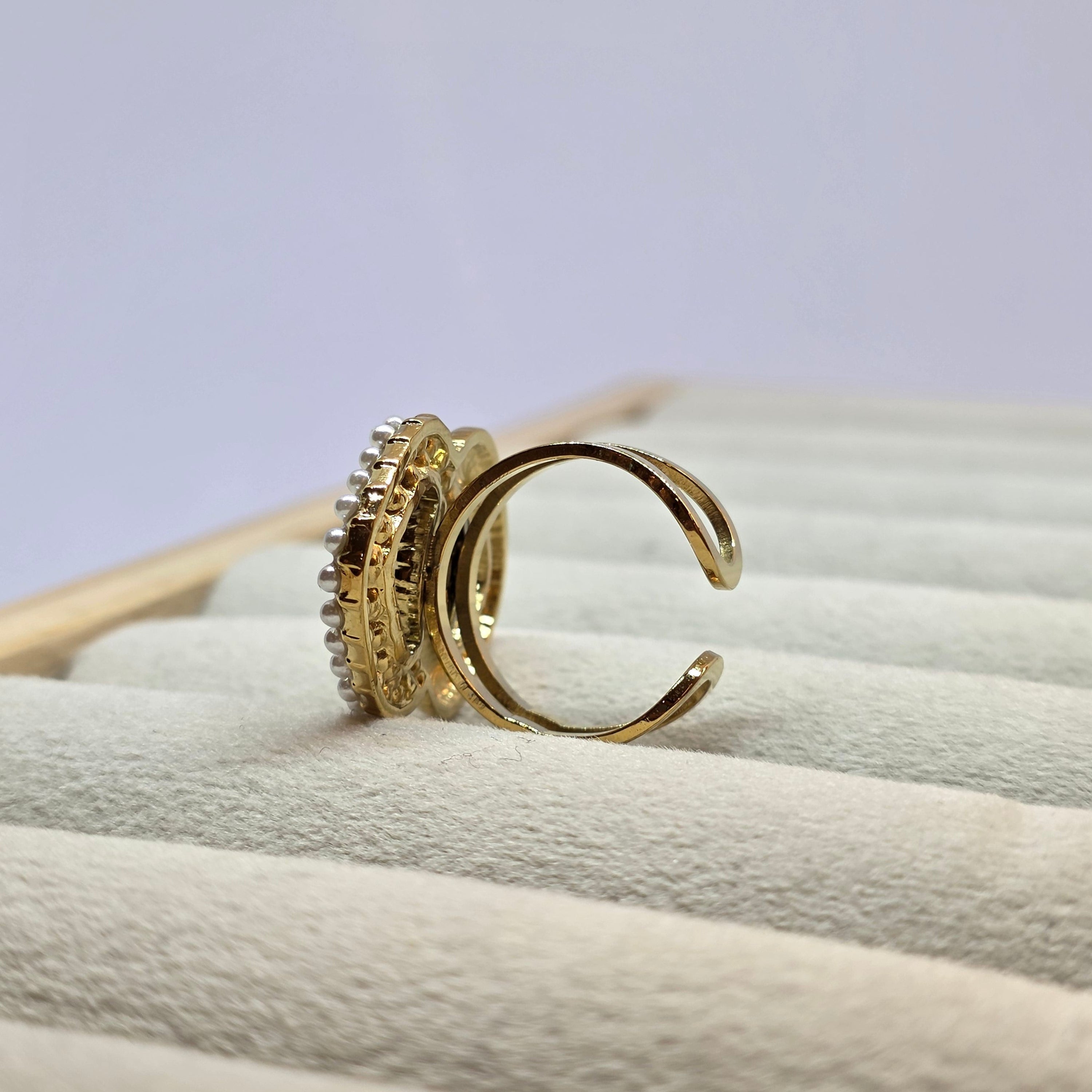 A pair of gold rings displayed on a cream-colored ring tree. One ring is a simple open-band hoop, and the other is a textured band set with small clear stones.