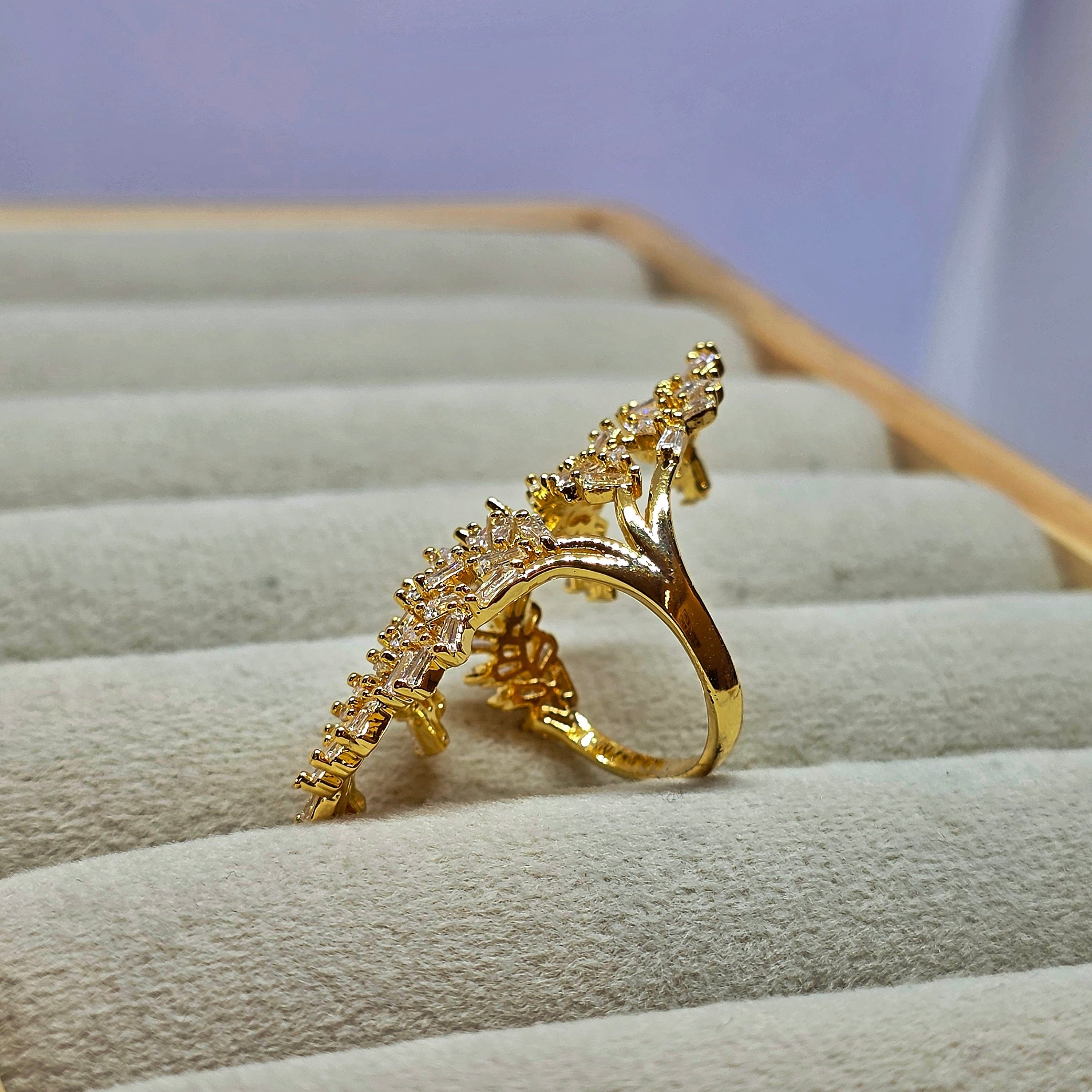 A gold ring with a highly textured, leaf-like or coral-like top setting, displayed on a beige velvet jewelry box.