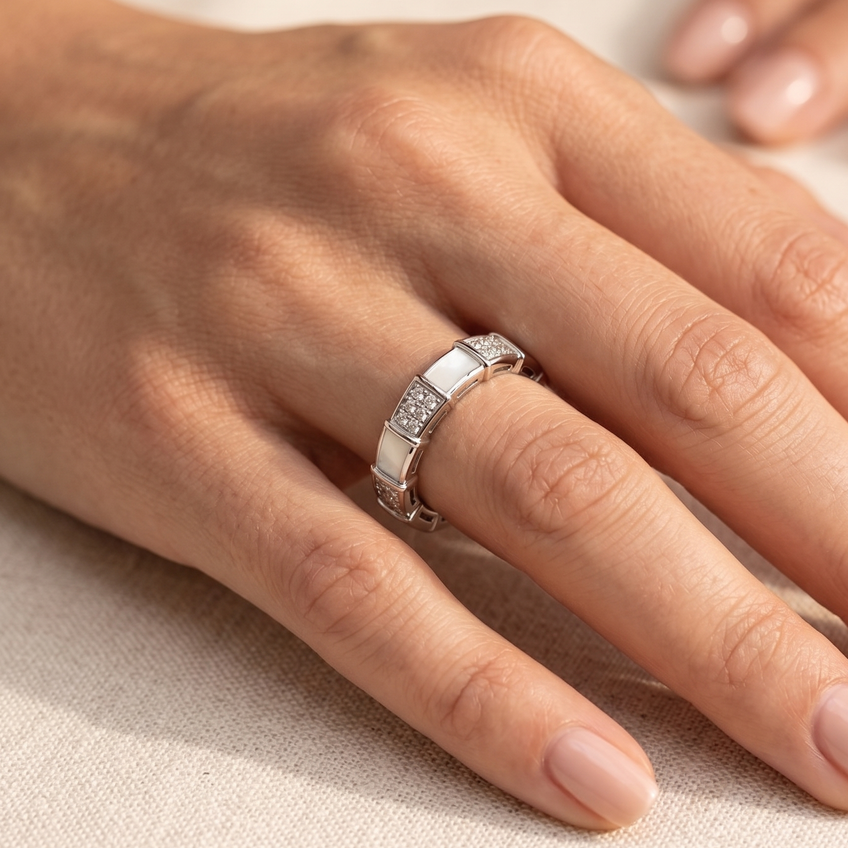 A silver ring with a textured geometric band and a small inset row of clear stones, shown worn on a hand against a neutral beige background.