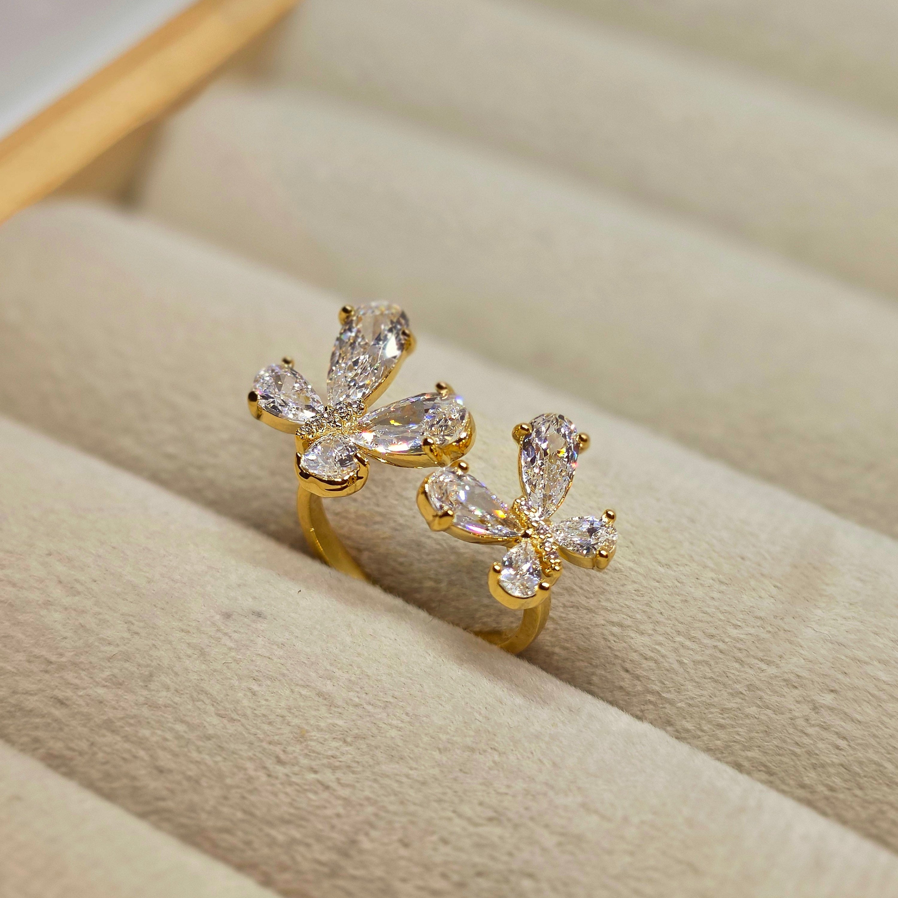 A pair of gold rings with marquise-cut clear crystals arranged on a beige jewelry display cushion.