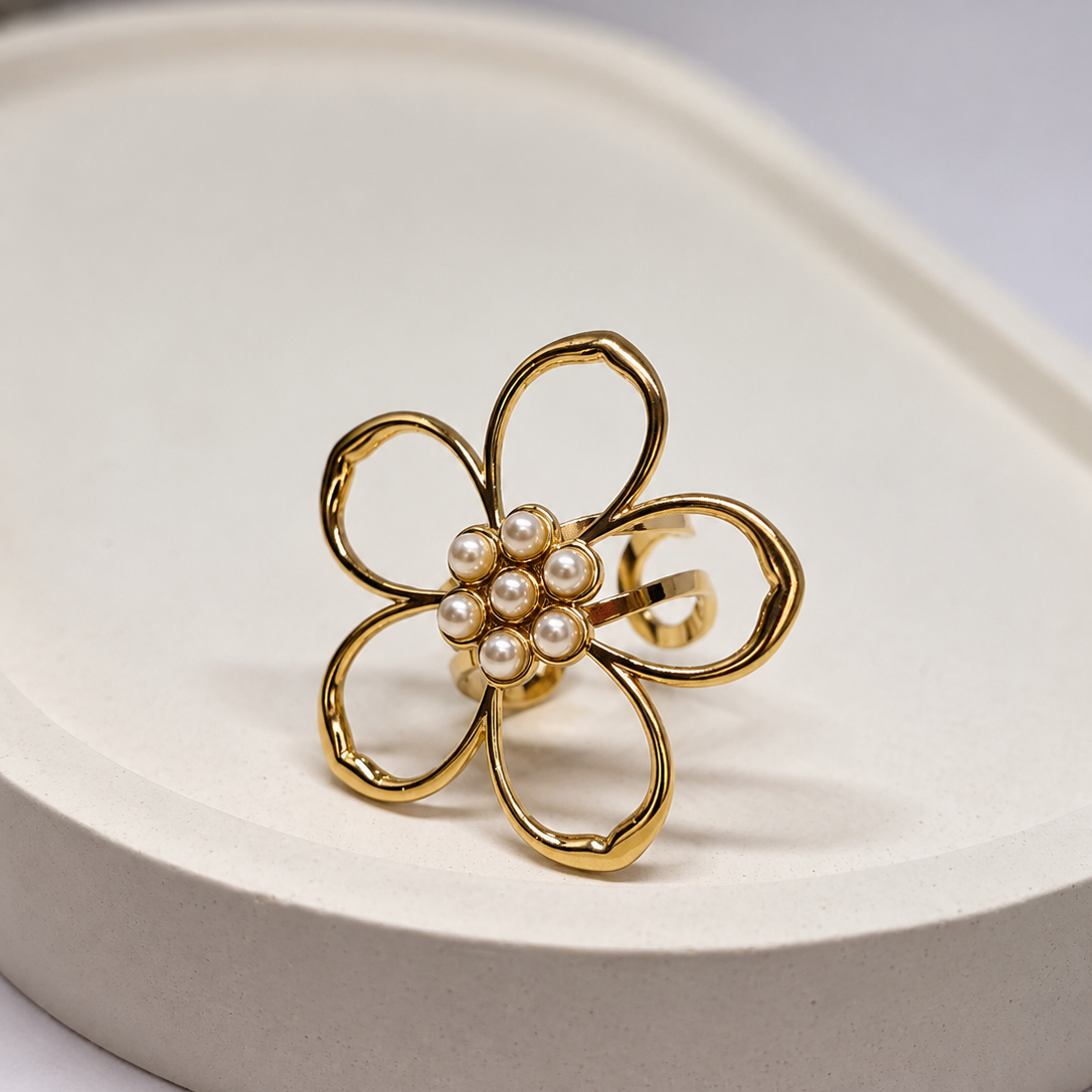 A gold flower-shaped hair claw clip with a cluster of small white faux pearls in the center, displayed on a light beige textured surface.