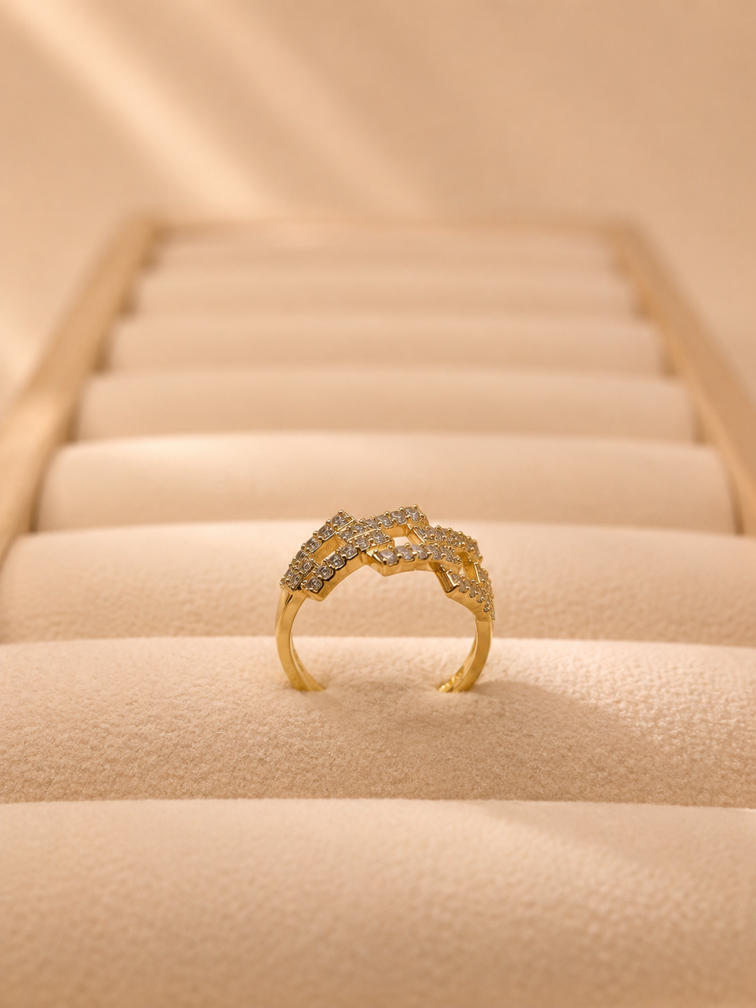 A gold ring with pavé-set clear stones, displayed on a cream-colored jewelry box cushion.