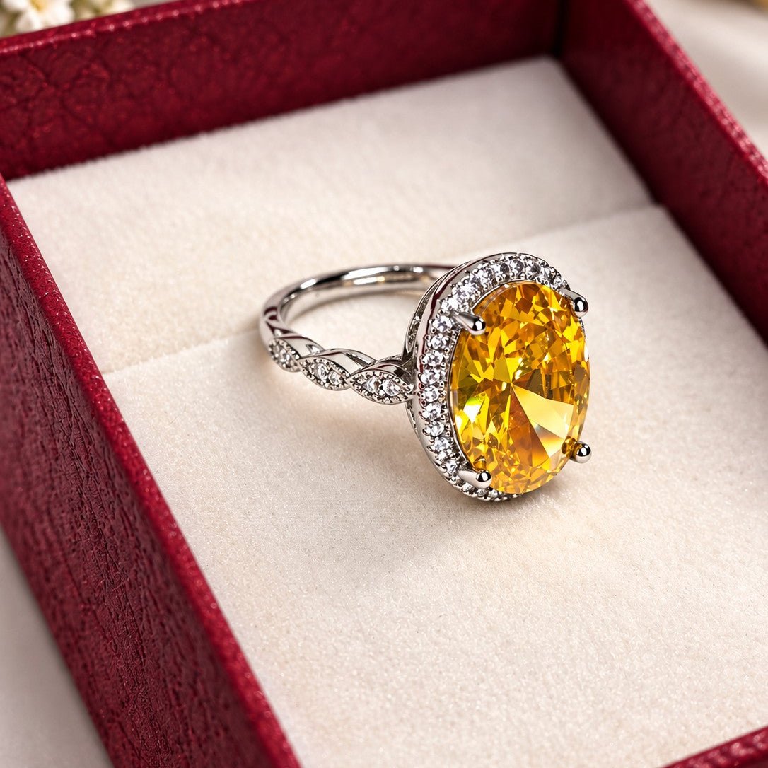 An oval yellow gemstone ring with a silver-toned halo and band, displayed inside a red jewelry box with a cream insert.