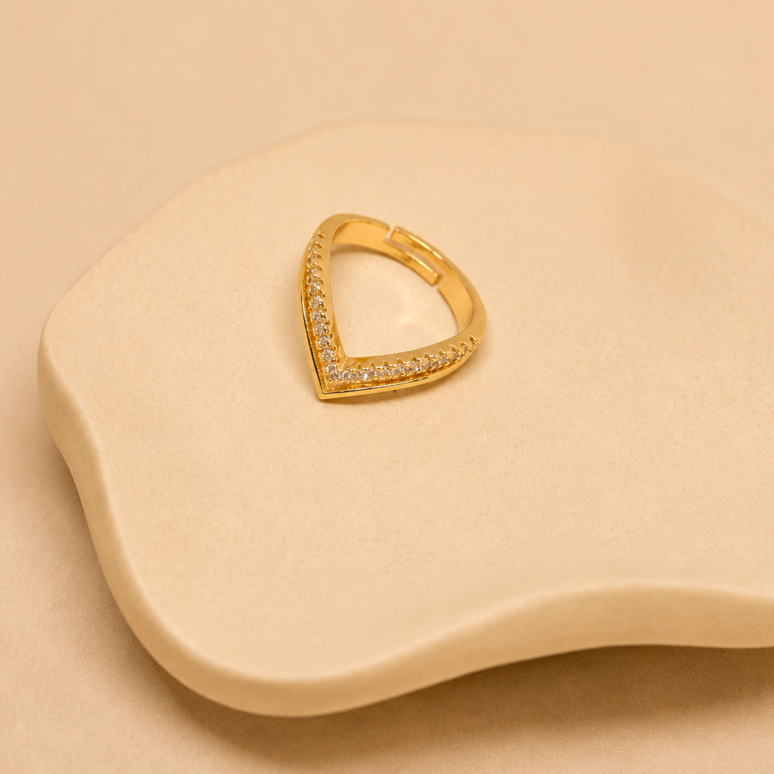 A gold triangular hoop earring with pavé-set clear stones, displayed on a beige wavy jewelry stand against a matching beige background.