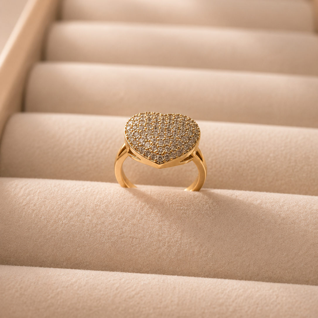 A gold ring with a textured, diamond-paved heart-shaped face, displayed on a beige velvet jewelry box.
