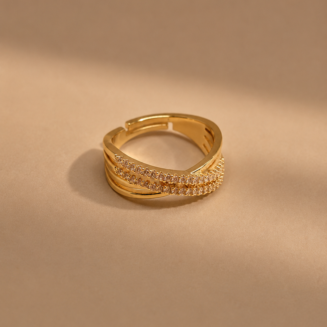 A gold-plated triple-band ring with two rows of small clear pavé stones on the front, displayed on a warm beige background with soft shadows.