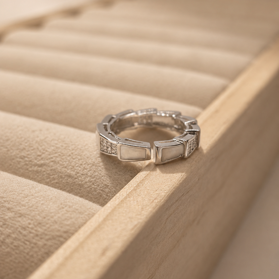 A silver ring with rectangular inlaid stones, resting on the edge of a beige jewelry box.