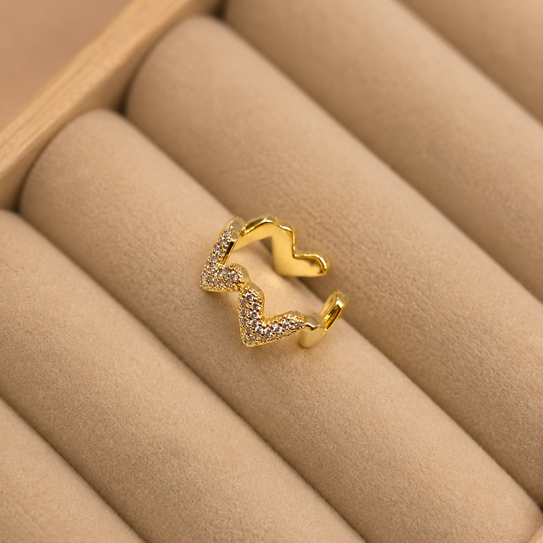 A gold-toned open ring with a wavy, zigzag design and pavé-set clear stones, displayed on a beige jewelry tray.