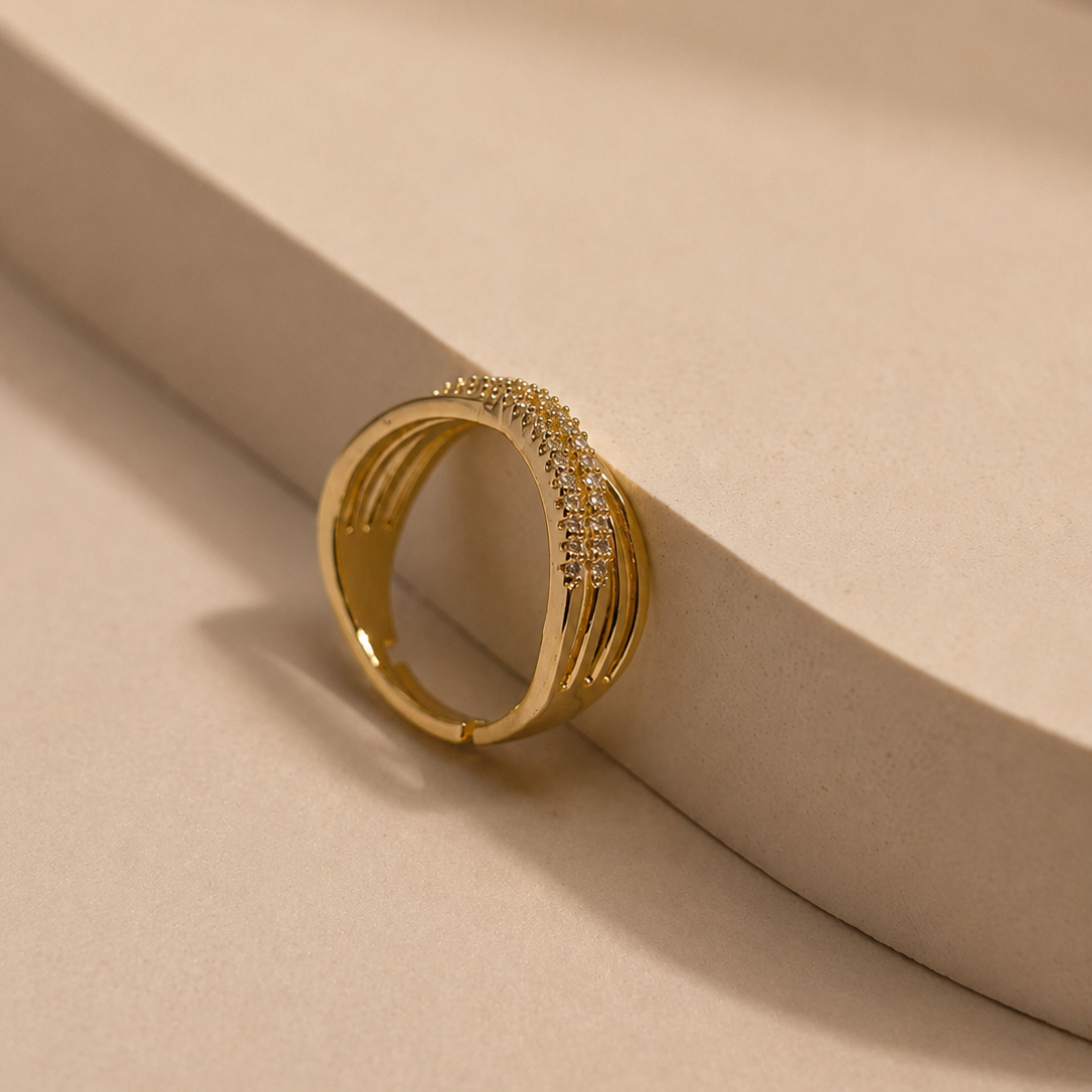 A gold-plated ring with a textured, ridged band and a top row of small clear pavé-set stones, resting on a beige geometric display stand.
