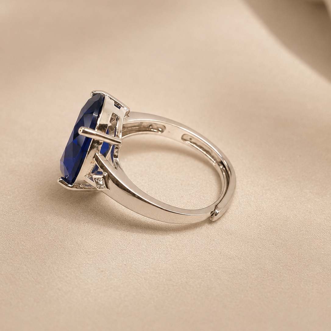 A silver ring featuring a rectangular deep blue gemstone in a prong setting, displayed on a soft beige fabric background.