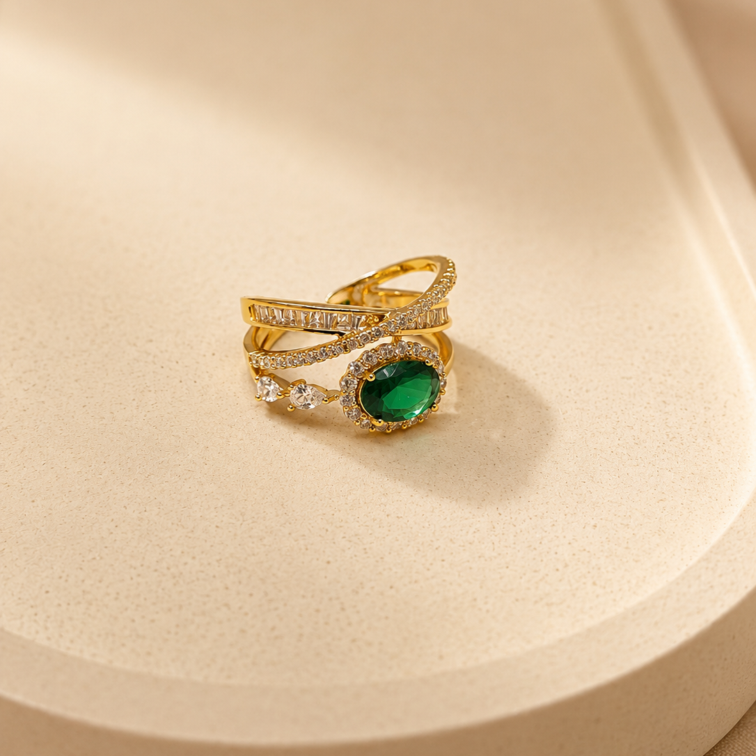 A gold ring with a green oval gemstone and small clear stones, displayed on a beige textured surface.