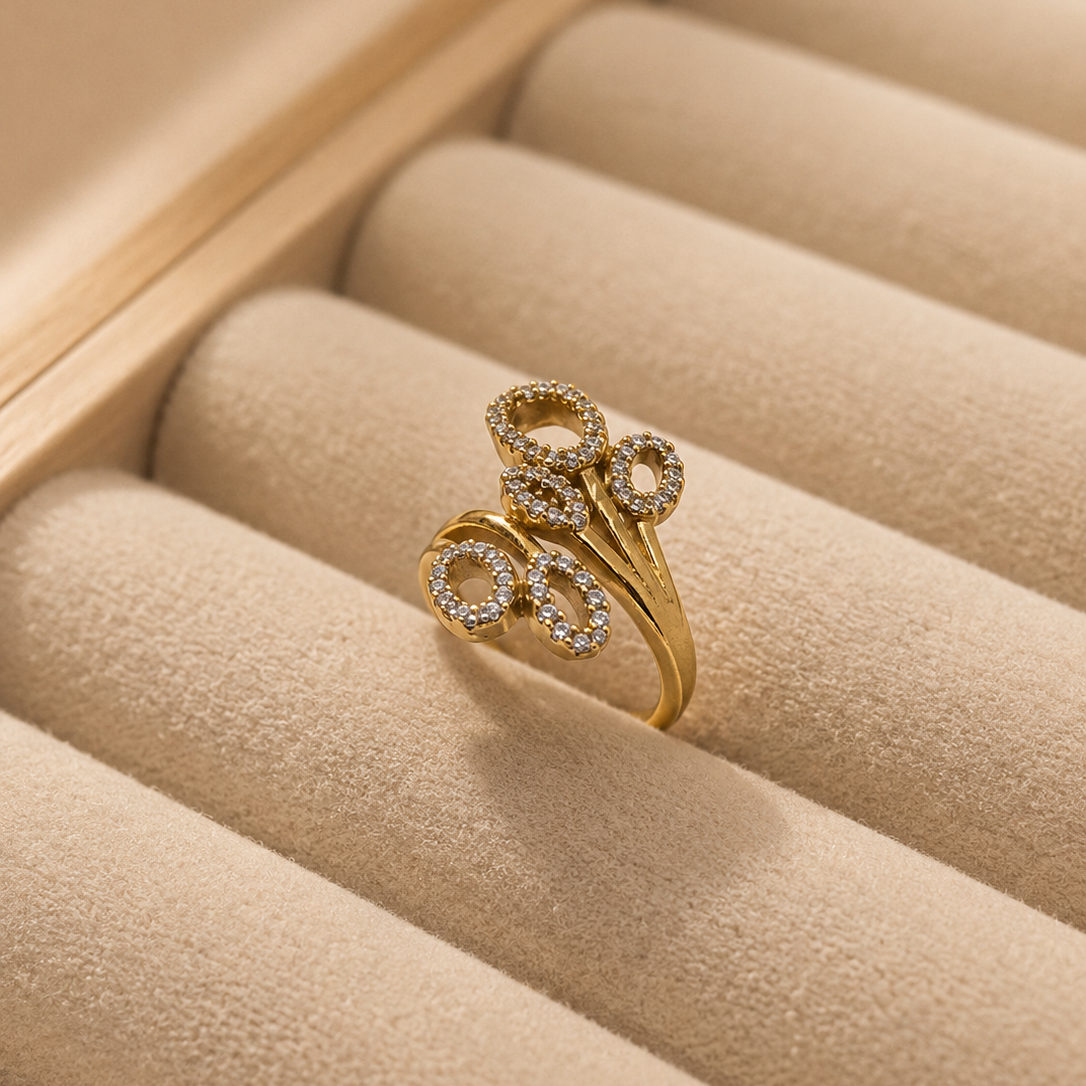 A gold ring with three interlocking oval motifs set with small clear stones, displayed on a beige jewelry tray.
