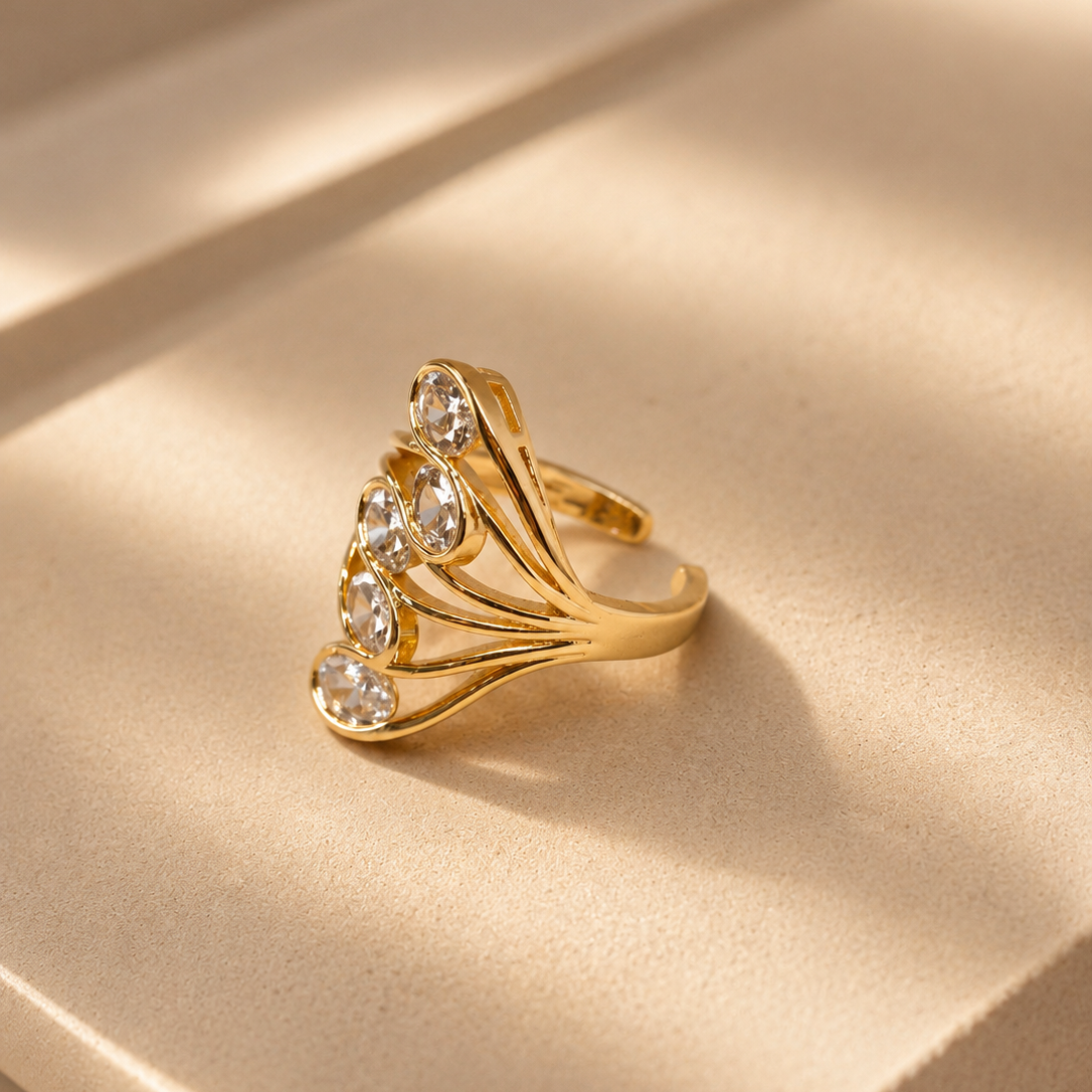 A gold ring with a fan-like cluster of clear round gemstones, displayed on a beige satin surface with soft shadows.