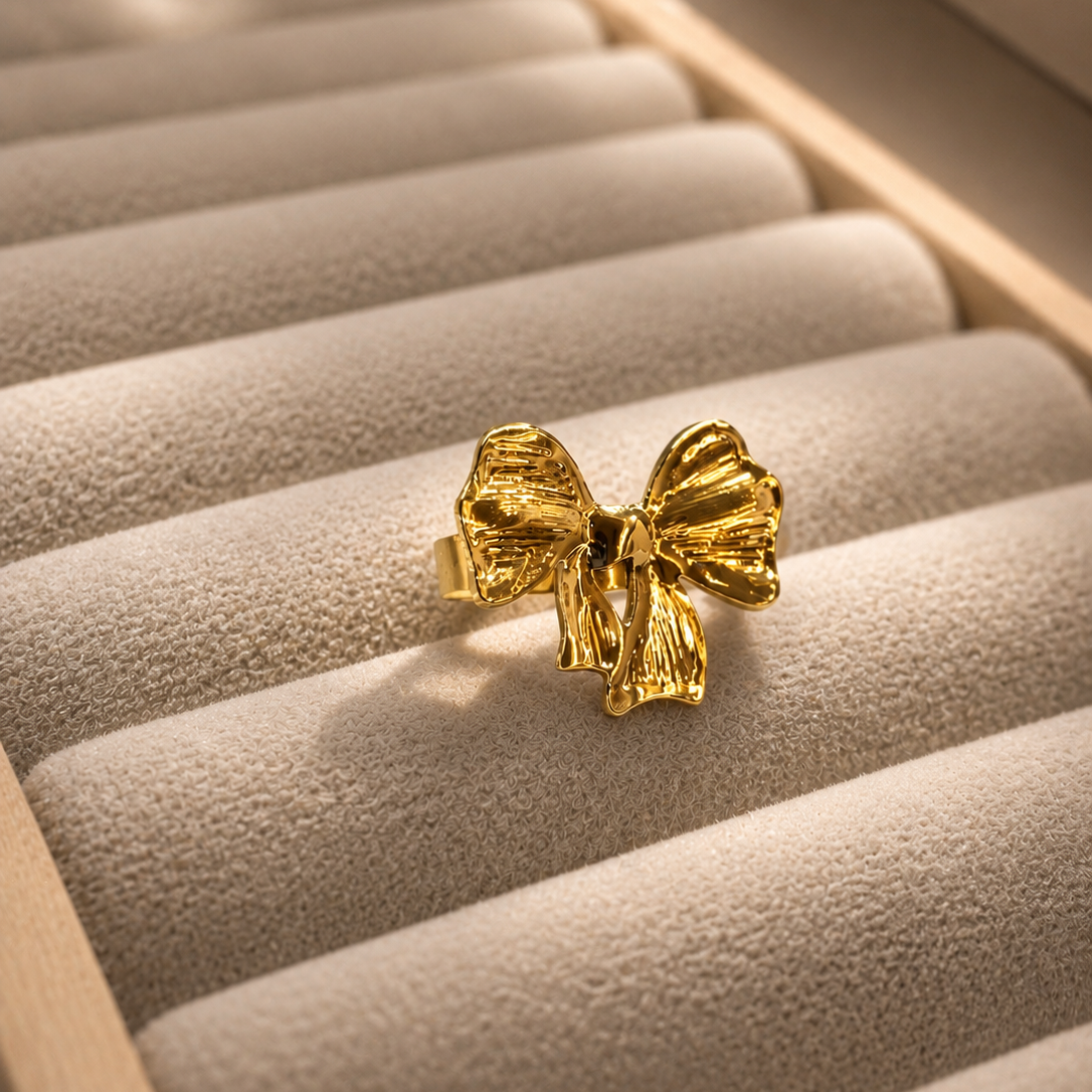 A textured gold bow ring displayed on a beige velvet jewelry box.