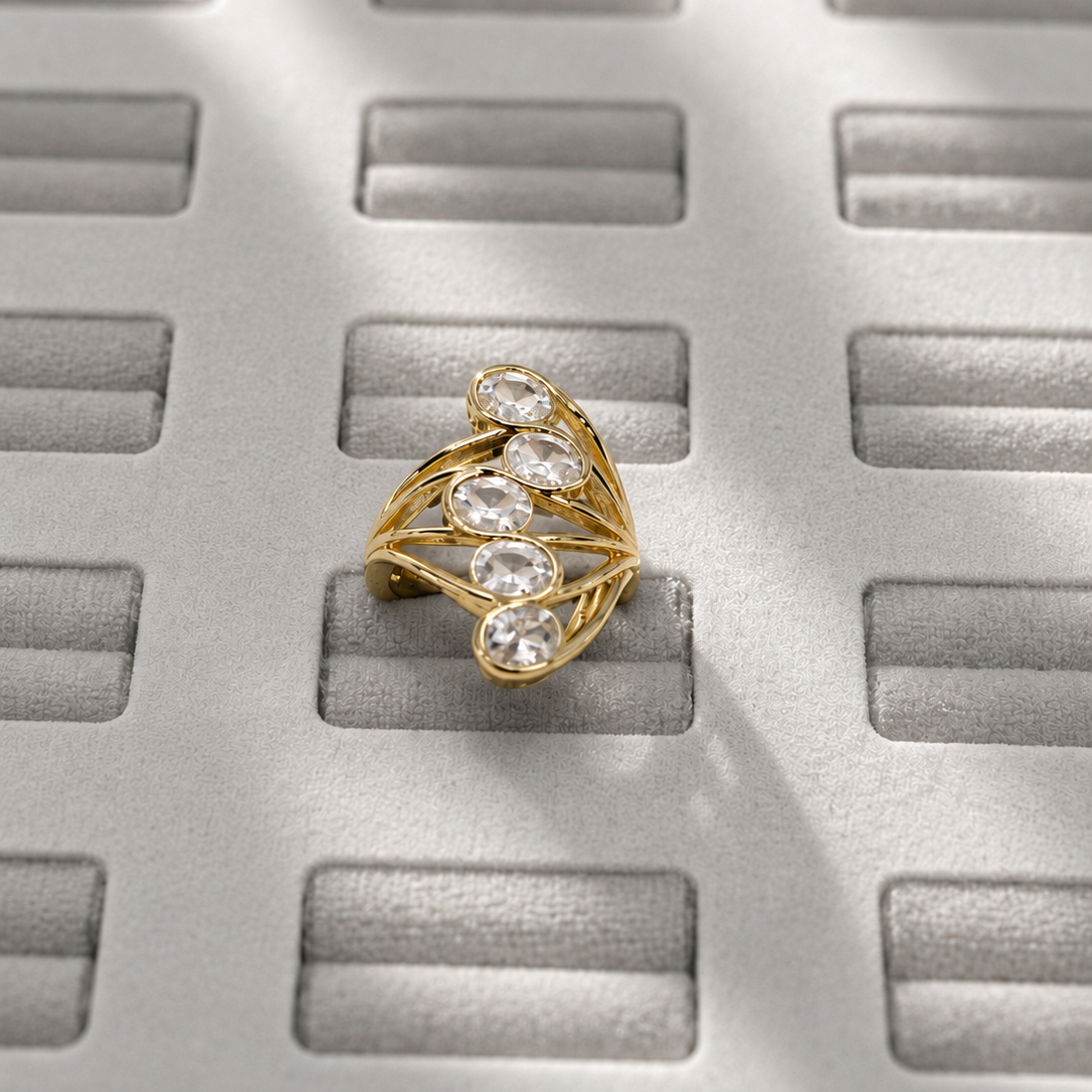 A gold ring with three clear marquise-cut gemstones, displayed on a textured gray surface with a grid pattern and soft shadows.