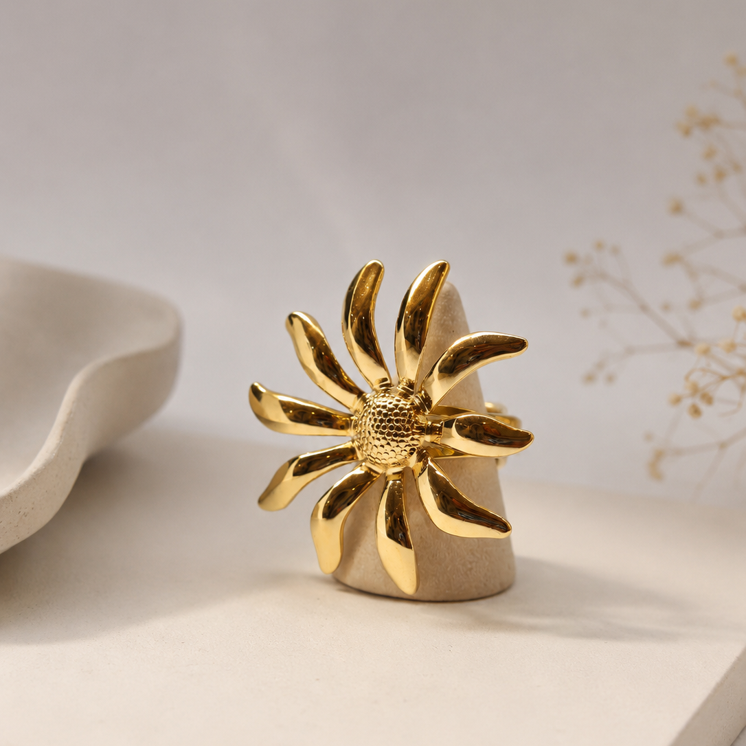 A gold flower-shaped ring displayed on a beige ceramic stand, set against a soft neutral background with minimalist props.